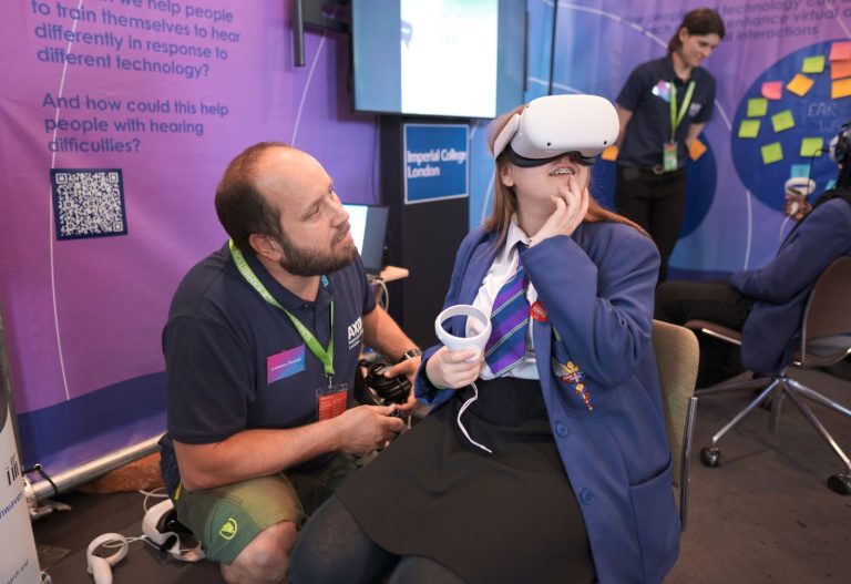 SONICOM PI Lorenzo Picinali crouching down next to a schoolgirl who is sat down wearing a virtual reality headset.